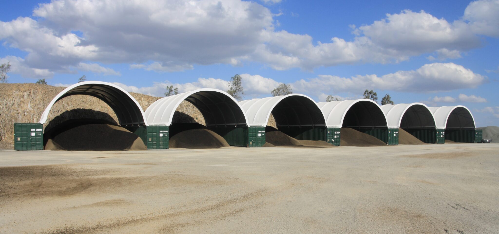 Multiple fabric shelters lined up, protecting stockpiles of materials, emphasising the capacity of fabric structures to provide shade and reduce heat exposure in work environments.