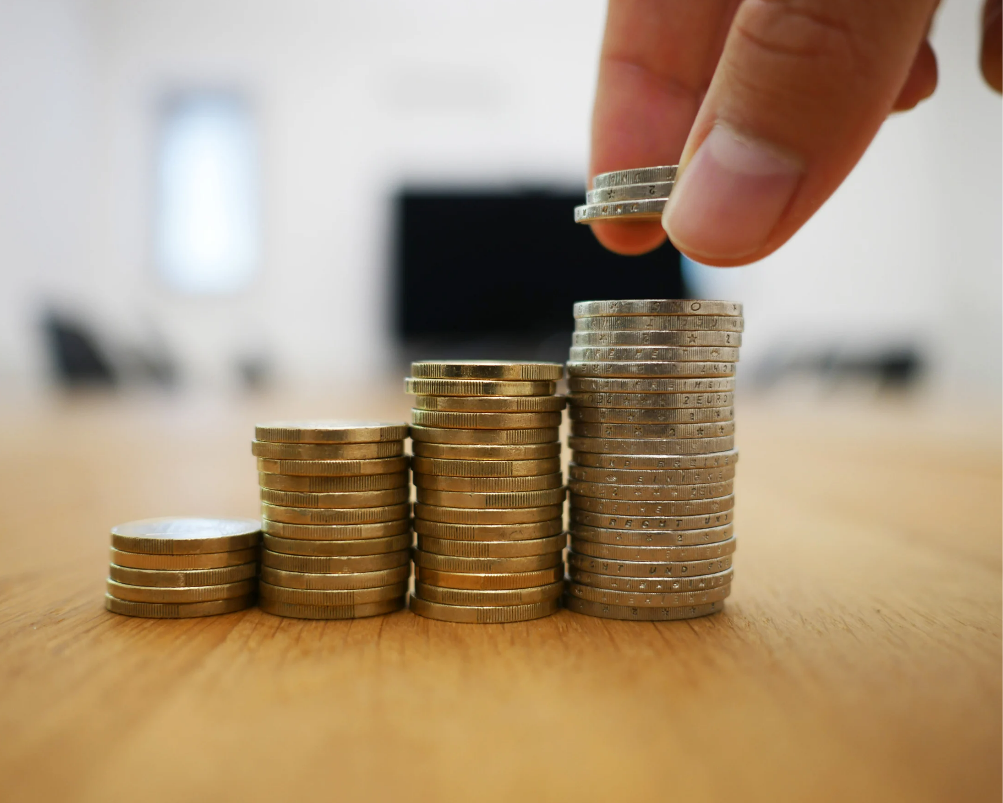 A hand stacks coins on a wooden table, illustrating financial growth.