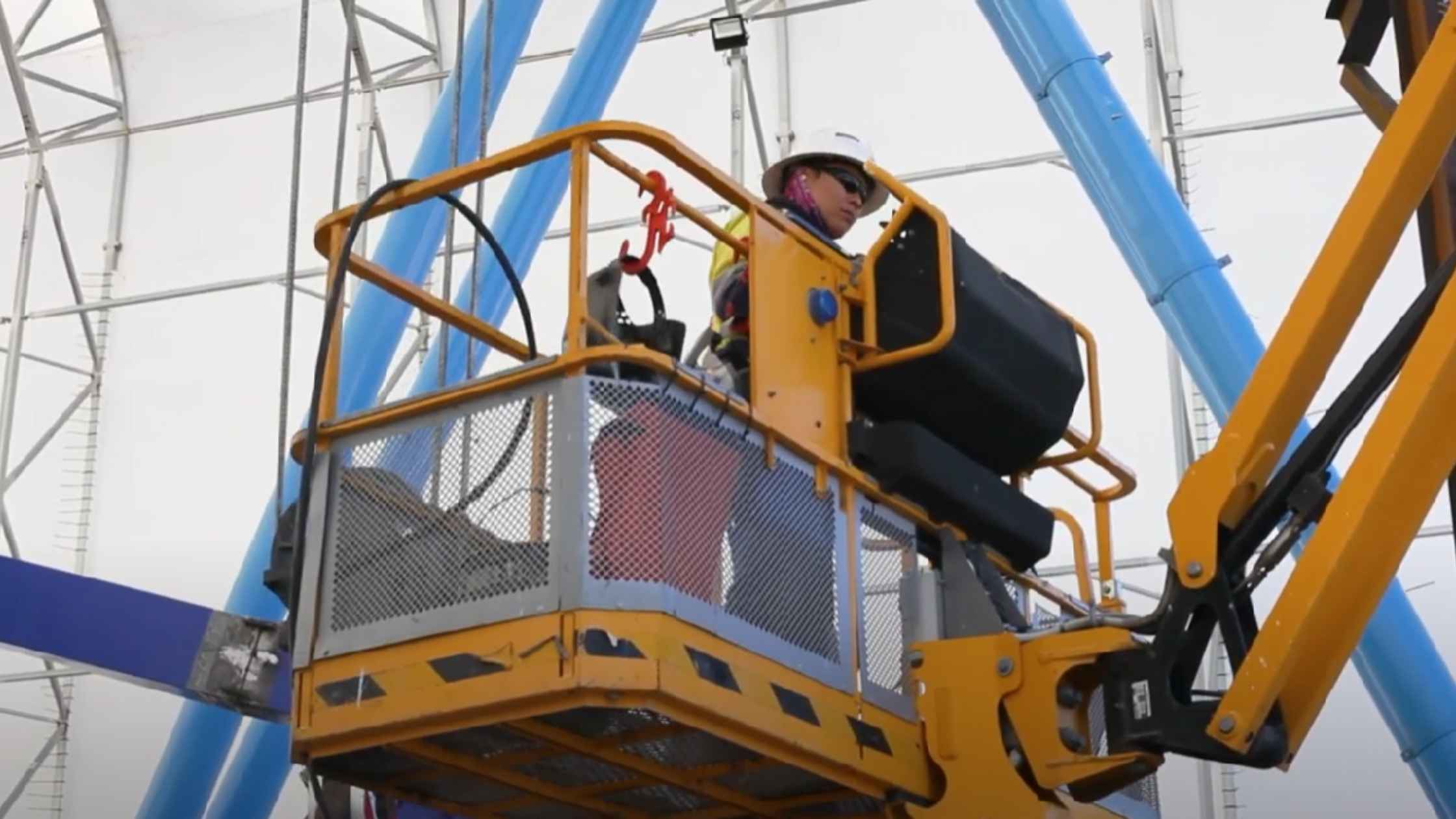 Worker conducting fabric shelter maintenance from elevated platform.